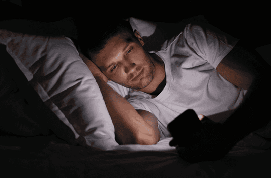 Man lying on bed in dark room looking at phone