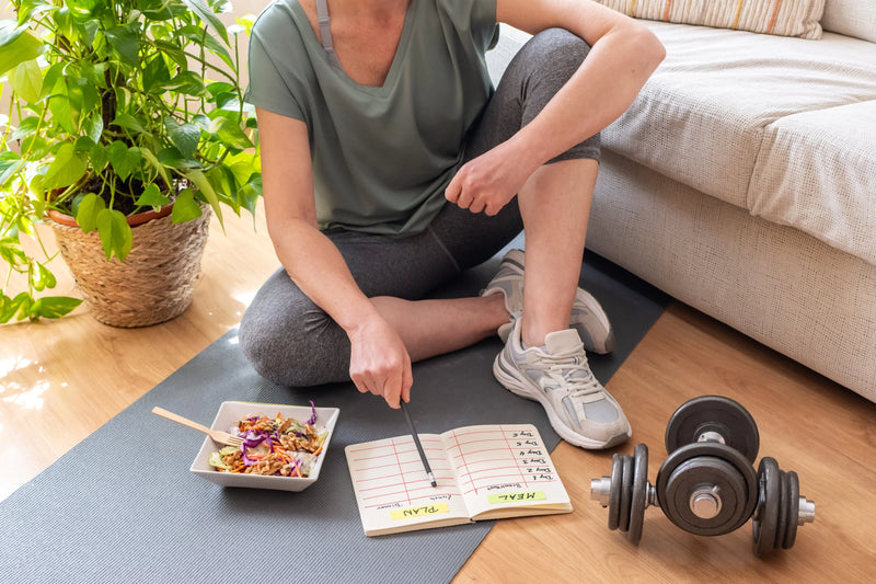 Woman sitting on the floor with healthy meal and planning her wellness routine